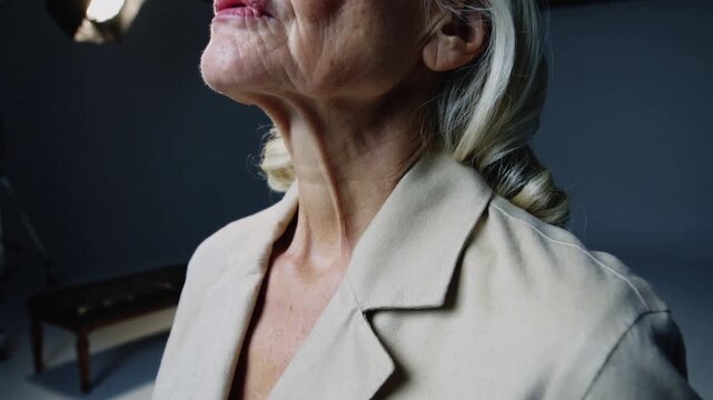 Following cue, senior woman raising and tilting chin for portrait at studio showing blazer