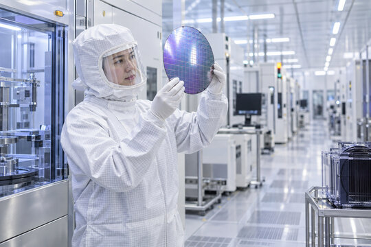 Engineer inspecting silicon wafer in semiconductor cleanroom