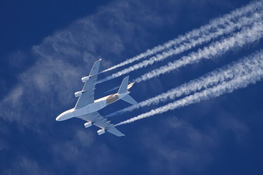 A majestic passenger airplane streaks across a vivid blue sky, leaving a trail of white contrails in its wake. ..Created with Generative AI, not depicting real subjects.