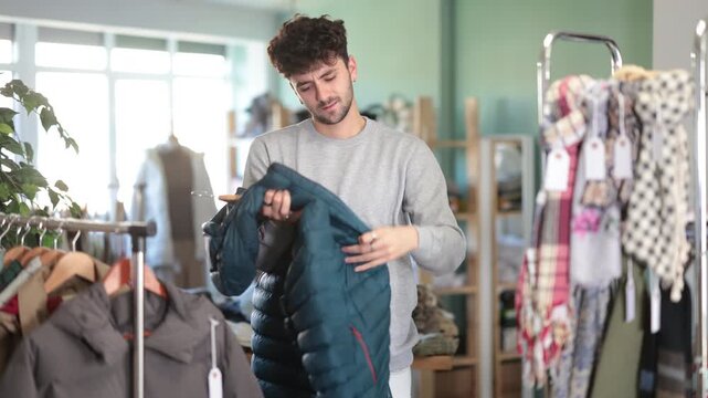 Undetermined young male customer looking for some puffer jacket in retail outlet 