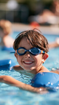 Portrait of a smiling boy in the swimming pool wearing goggles and inflatable arm sleeves, summer travel hotel vacation or swim class concept, with copy space