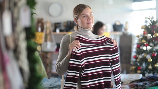 Woman buys knitted wool sweaters at bargain prices at a New Year sale. Christmas shopping before the holidays 