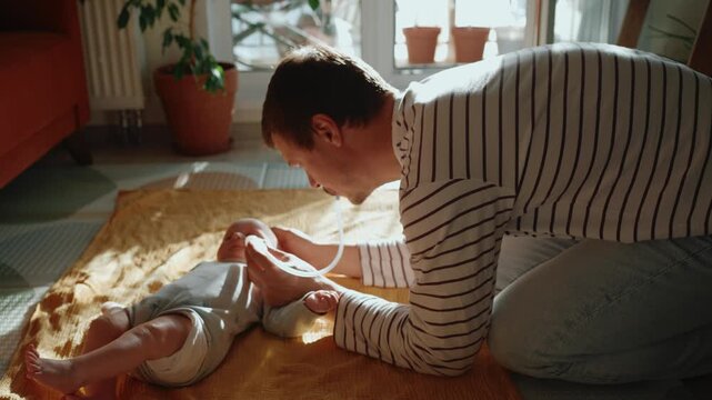Careful father kneeling on the floor, using a snot sucker to help his newborn child breathe easier. Devoted dad providing healthcare and relieving his infant's nasal congestion at home