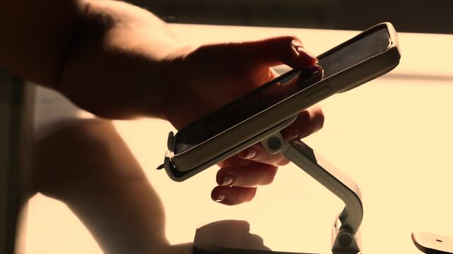 Sunlit hand reaches for mobile device mounted at desk corner