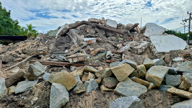 Pile of concrete debris broken stones and building rubble scattered outdoors under a cloudy sky.