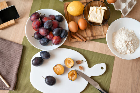 Ripe fresh whole and sliced plums on cutting board, eggs, flour, butter on kitchen table. Food ingredients for homemade famous plum pie cooking recipe