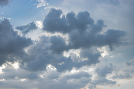 Dramatic cloudscape with blue sky and sunlight breaking through layered storm cloud, creating moody natural atmosphere and expansive weather background