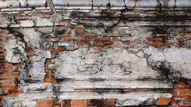 Old weather-worn cracked concrete and red brick wall texture background of an ancient Thai temple ruins.