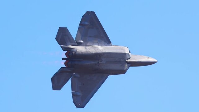 American f22 raptor stealth fighter jet flying high speed performing dynamic aerial maneuver in clear blue sky.