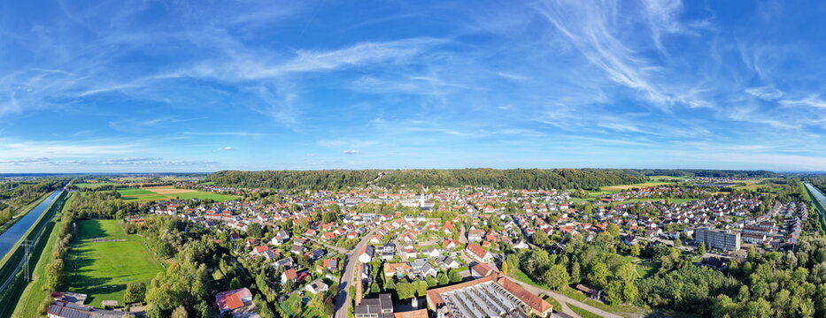 Panorama-Luftaufnahme von Altenstadt an der Iller mit Wohnh&auml;usern, gr&uuml;nen Feldern und blauem Himmel mit Schleierwolken an einem sonnigen Tag.