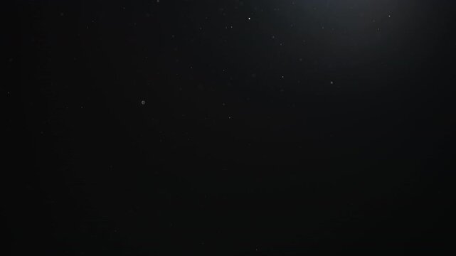 Slow motion of dust particles floating mid air over dark background with some lens flare