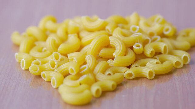 A pile of dry yellow elbow macaroni pasta placed on a smooth wooden surface