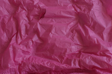 Obraz premium A close-up view of creased and crumpled dark pink wrapping tissue paper, showing detailed wrinkles and folds with a small tear
