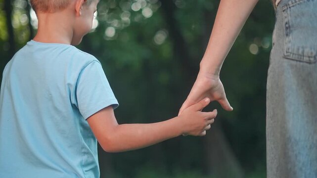 Boy walks beside parent holding hand. Parent supports boy during outdoor walk. Walk brings trust and care. Boy trusts hand that guides. Hand and walk help boy feel love and calm outdoors with parent