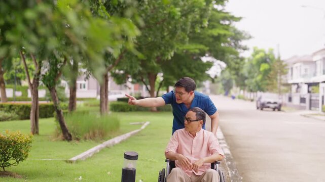 Asian male caregiver pushing senior man in wheelchair for outdoor walk near home, talking and spending time together, elderly mental health care, companionship, mobility support and home healthcare