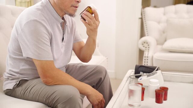 Asian senior man taking medicine from pill bottle at home, elderly healthcare with medication management, daily treatment and prescription drugs, health support and chronic disease care.