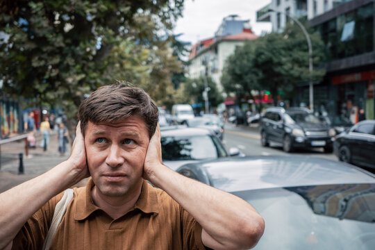 Sound sensitivity, overwhelmed man blocking ears in busy city traffic, sensory overload, auditory discomfort, difficulty focusing, mental wellbeing, stress reaction.
