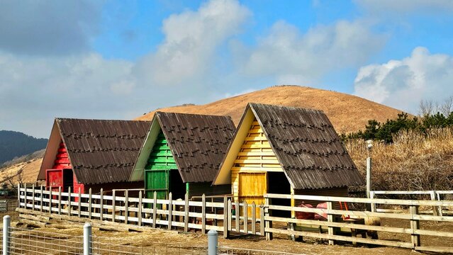 Colorful triangular wooden huts lined up on a ranch against scenic hills and blue sky