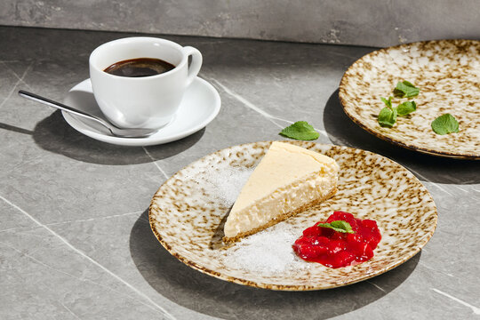 Slice of New York cheesecake with berry coulis and a cup of black coffee on a grey table with copy space
