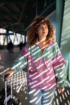 White woman walking and pulling suitcase in sunlit corridor in Spain