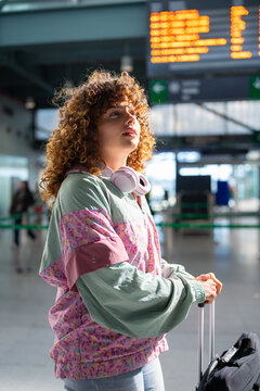 Young white woman waiting in train station with luggage and headphones
