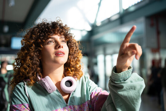 White woman with curly hair pointing inside modern indoor space