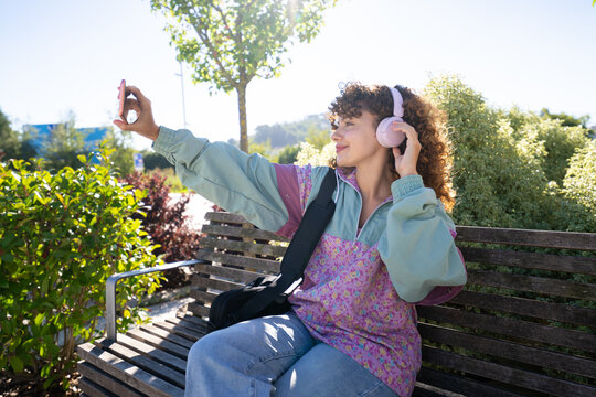 White woman taking selfie with pink headphones on wooden bench