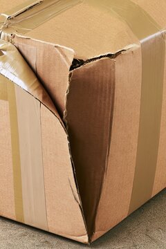 Damaged cardboard box with torn edge and creased surface in indoor setting