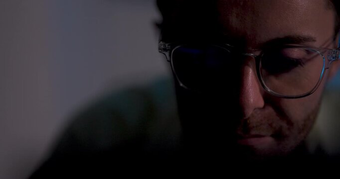 Adult male technology professional wearing glasses studies computer monitor, shifting gaze downward and across screen while reviewing software data during detailed digital system analysis in office.