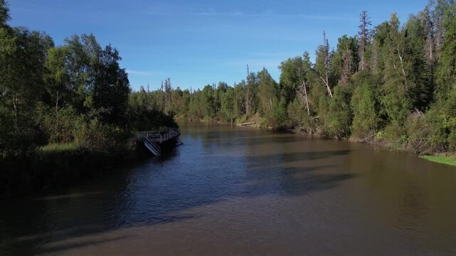 Low-altitude aerial flight along the Little Susitna River passing a fishing platform, rounding a river bend, and flying directly over a fisherman standing in the water. 1920x1080, 24fps