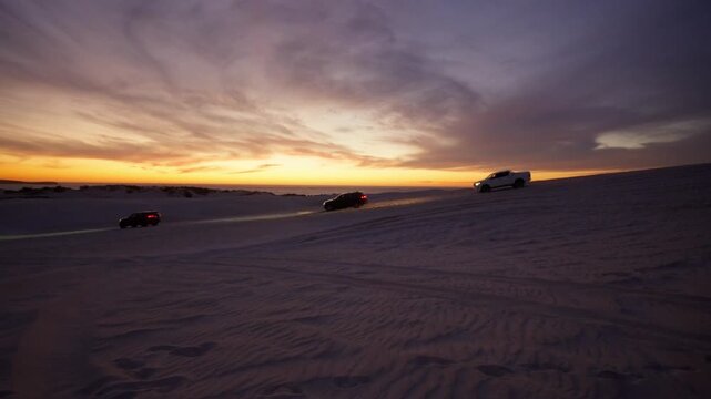 Three 4x4s driving along a dune at sunset, Lancelin Dunes, Australia