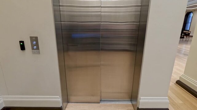 Woman entering modern steel elevator and pressing button for second floor inside professional office building.