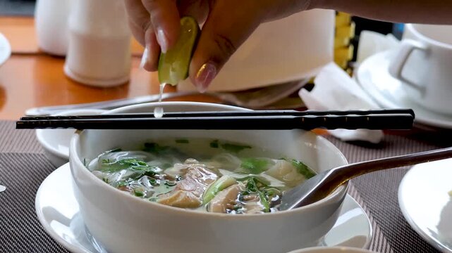 Close up of preparing pho soup adding lime and chili slices for delicious meal.