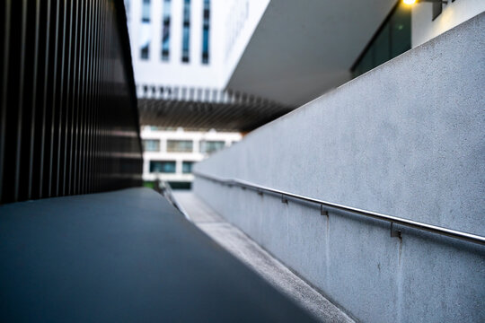Minimalist concrete ramp with long handrail and converging lines, creating strong perspective through a modern architectural walkway and access passage
