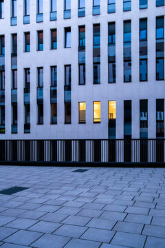 Blue modern building facade with repetitive vertical windows and isolated warm lights, forming a geometric architectural pattern in a quiet exterior