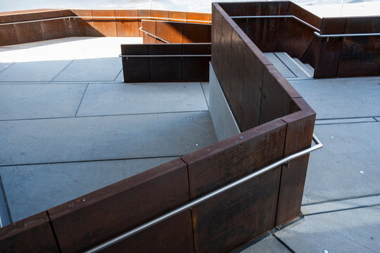 Geometric architecture detail with concrete walkway, metal ramp and handrail forming minimalist lines across an exterior circulation space