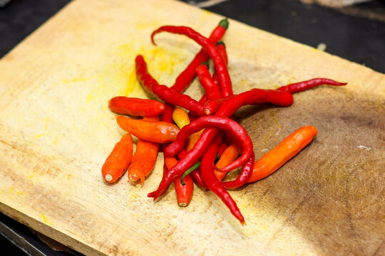 A pile of fresh red and orange cayenne chili peppers placed on a wooden cutting board