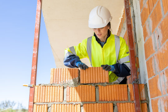 Female mason placing ceramic block on wall with precision