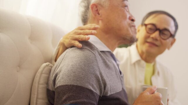 Happy Asian senior gay couple drinking coffee and talking together at home in the morning. Elderly lgbtq family enjoying companionship, bonding, conversation and relaxed retirement healthy lifestyle