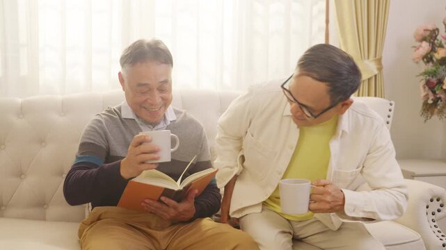 Happy Asian senior gay couple drinking coffee and talking together at home in the morning. Elderly lgbtq family enjoying companionship, bonding, conversation and relaxed retirement healthy lifestyle