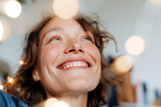 Joyful Woman Laughing with Bokeh String Lights in Cozy Home Interior