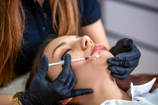 Plastic surgery. Young woman receiving injection in the chin at beauty clinic, closeup. Beauty treatment of face correction. Cosmetologist making filler injection in female chin
