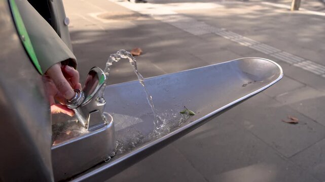 Person pressing button on water fountain outdoor, water spraying in slow motion.