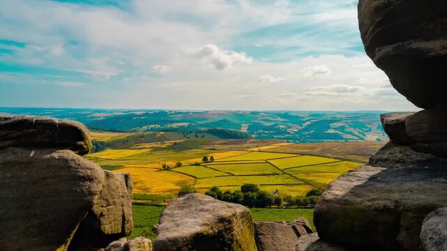 Timelapse Gritstone rocks around agricultural valley under blue sky with clouds. Farmland divided by dry stone walls beneath open countryside horizon time lapse. Rural fields distant hills rock