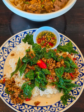 
A Thai meal of minced-beef pad krapow piled over jasmine rice with holy basil and chilies, plus nam pla prik on the side and a bowl of spicy beef sap soup in the background.