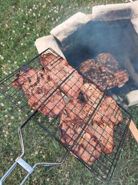 Juicy meat steaks grilling on wire grate over open brick fire pit for outdoor summer barbecue and family picnic concept