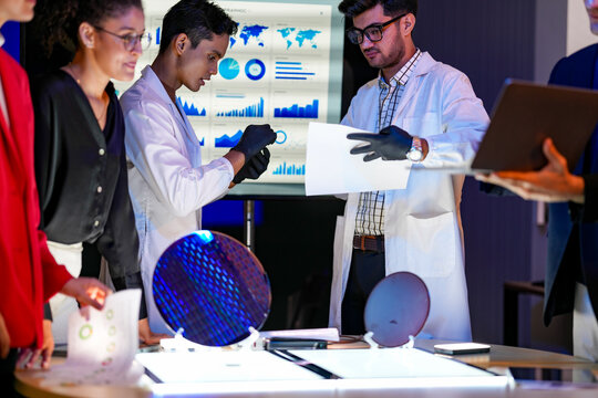 An engineer checks the wafer against the printed test report with the wafer standing on the bench and a laptop open beside it and the cause is found in a research laboratory