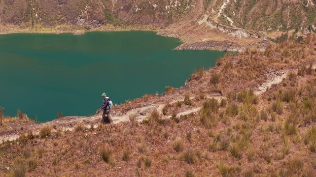 Lone traveler hiking on a narrow path along the shore of a beautiful turquoise mountain lake