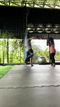 Vertical video of a man and hijab-wearing woman practicing kickboxing sparring and martial arts techniques in a modern gym.