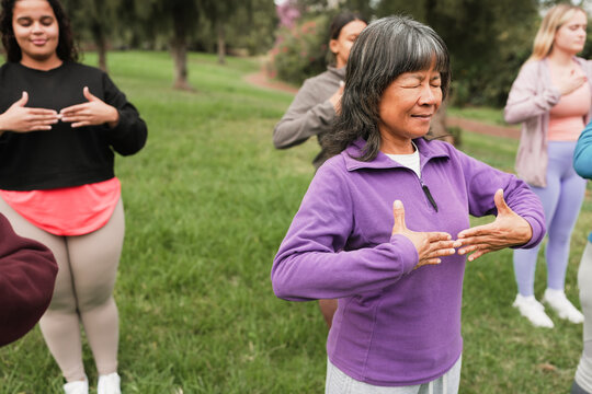 Group of women doing meditation class with people of different age and body type - Healthy lifestyle and meditation concept - Main focus on center asian woman face